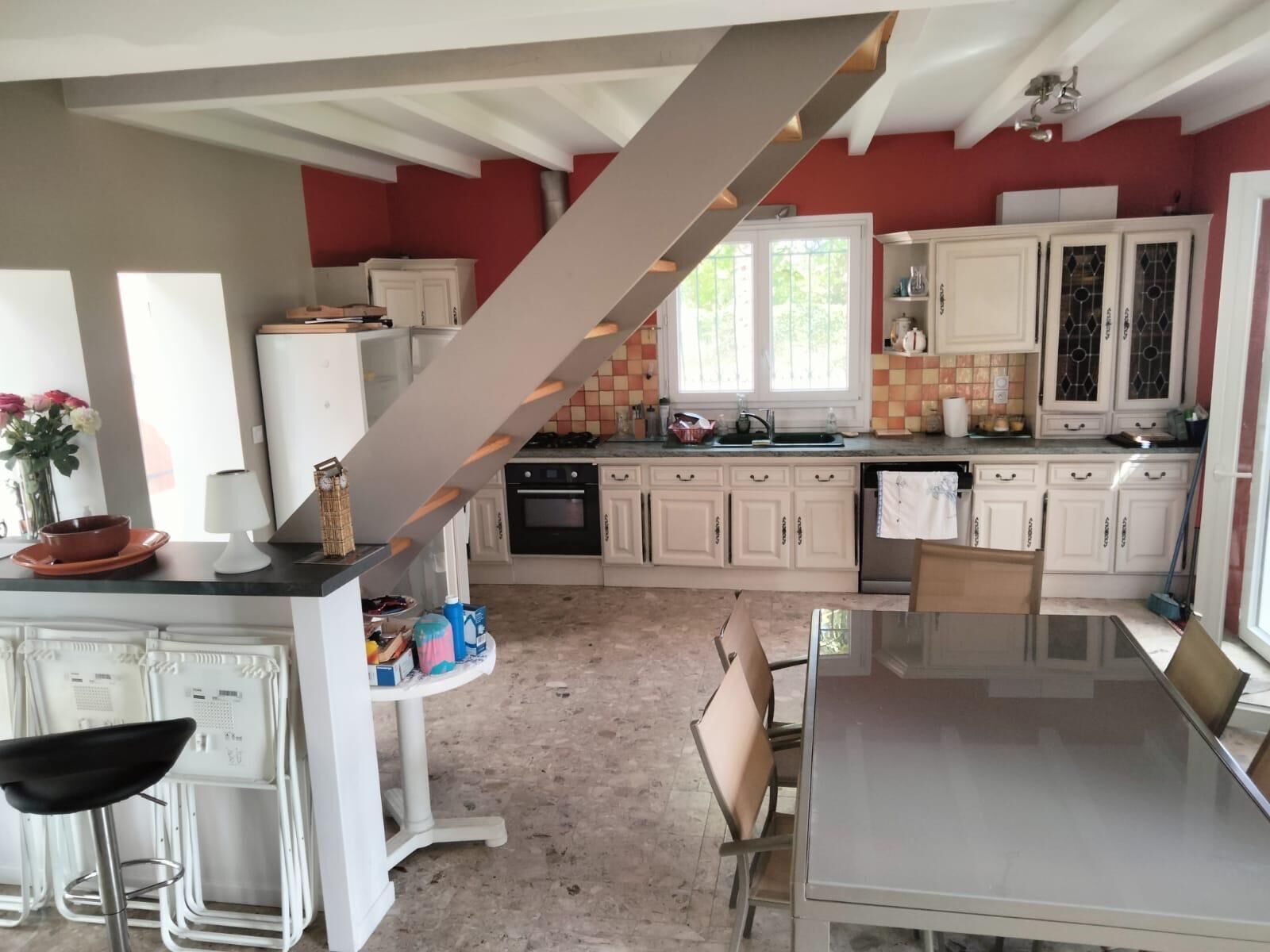 Une cuisine avec des meubles blancs, une table à manger et un escalier.