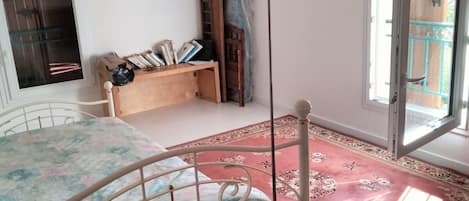 A bedroom with a bed, a bedside table, a lamp, a window, and a door.