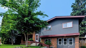 Une maison à deux étages, dotée d’un mur de soutènement en pierre, d’une pelouse devant et surplombée d’un ciel bleu dégagé.