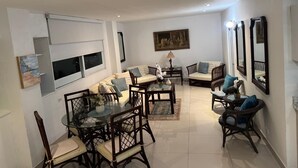A living room with a sofa, chairs, a dining table, and a painting on the wall. - Your home by the Beach! 2bedroom penthouse apartment in Isla Verde, PR (Carolina)