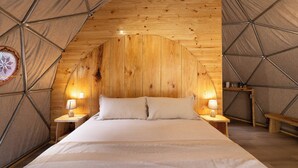 A cozy, arched wooden tent-style room with a bed, two bedside lamps, and a small wooden bench.