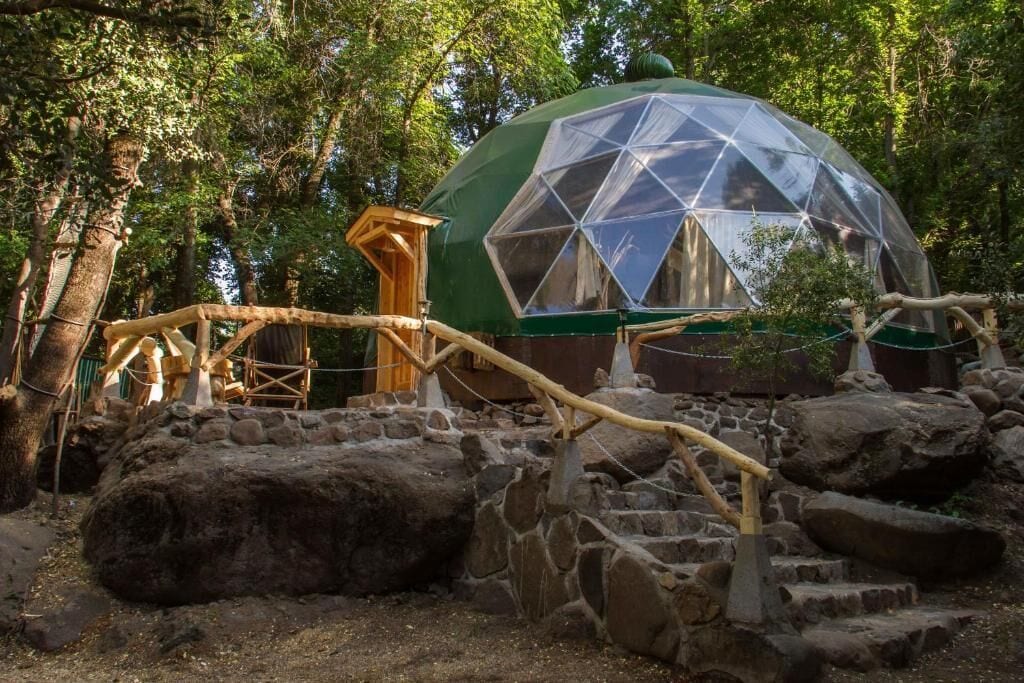 Estrutura em forma de cúpula geodésica rodeada por formações rochosas naturais e árvores.
