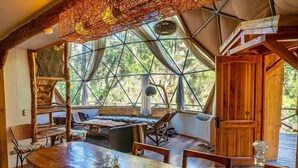 A wooden dining table with chairs, a chandelier, and a large window with a view of trees.