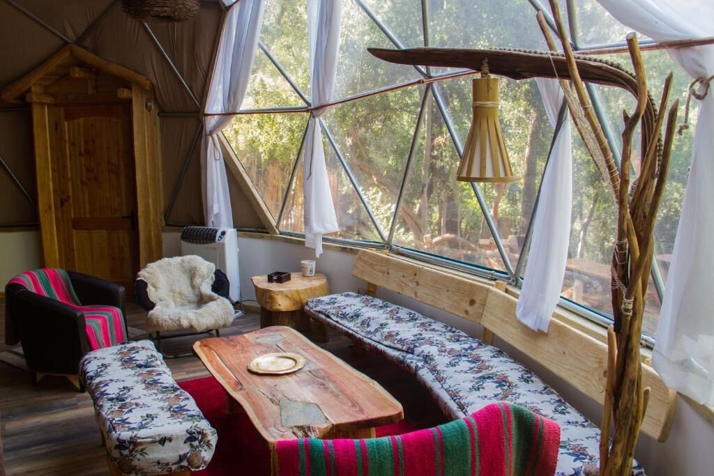 Un interior acogedor con un banco de madera, una mesita, un sillón de piel y un ventanal con vistas a árboles.