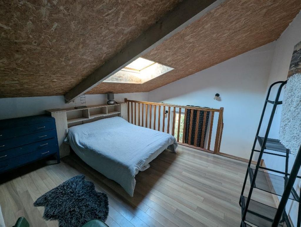 Una camera da letto con soffitto spiovente, un letto, un comò, un lucernario e una scala.