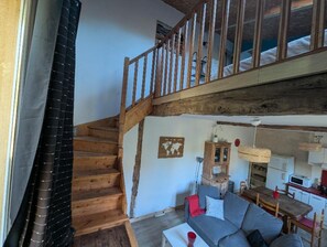A loft-style living space with a wooden staircase, a sofa, a dining table, and a kitchen area.