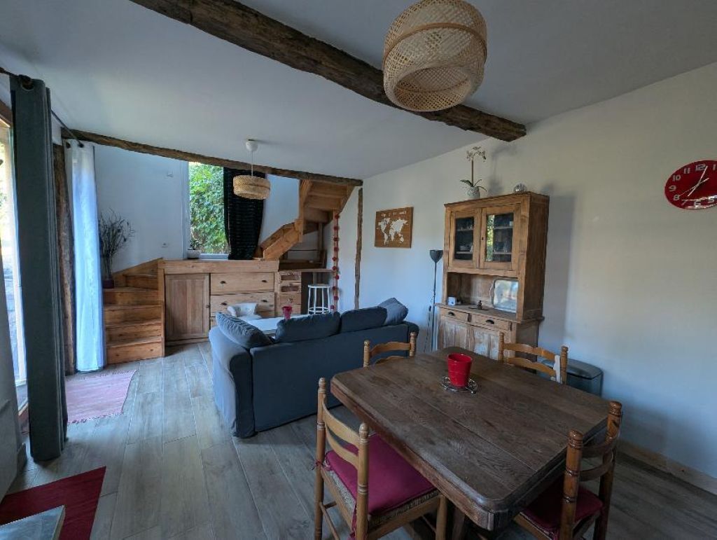 A cozy living room with a wooden dining table, a sofa, and a staircase leading to an upper level.