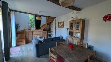 A cozy living room with a wooden dining table, a sofa, and a staircase leading to an upper level.