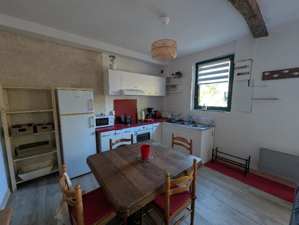 A compact kitchen with white cabinets, a wooden dining table with chairs, and a red rug.