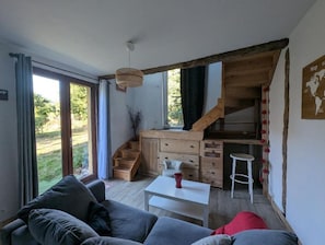 A modern interior with a sofa, a small table, a kitchen area with wooden cabinets, and a staircase leading to an upper level. - Vrbo Property (Cintré)