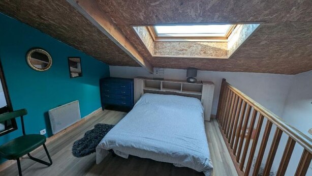 Een slaapkamer met dakraam, een bed, een stoel en een blauwe muur.