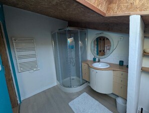 A bathroom with a glass shower enclosure, a sink with a mirror, and a towel rack. - Vrbo Property (Cintré)