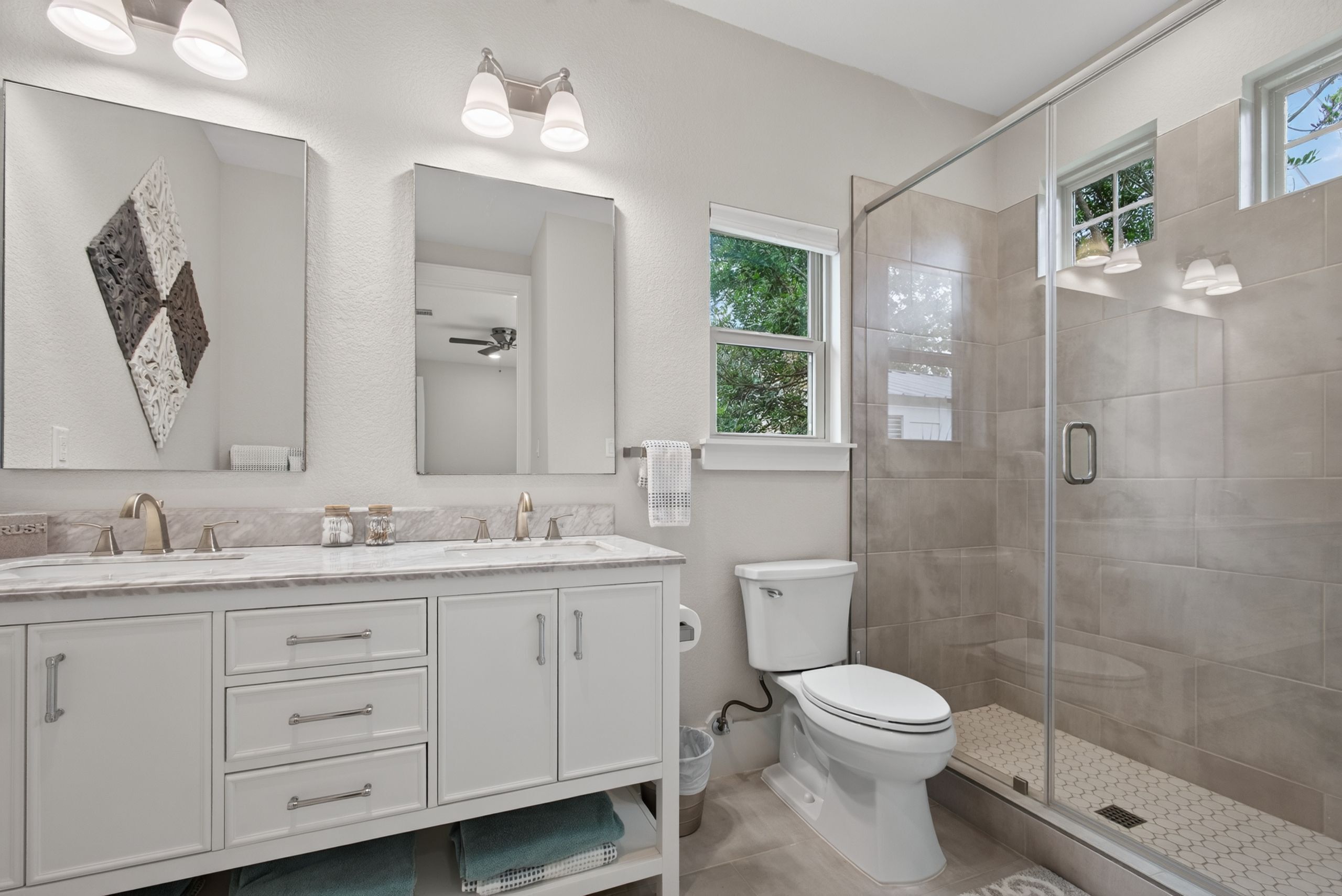 A bathroom with a shower, toilet, and vanity with a mirror and lights.