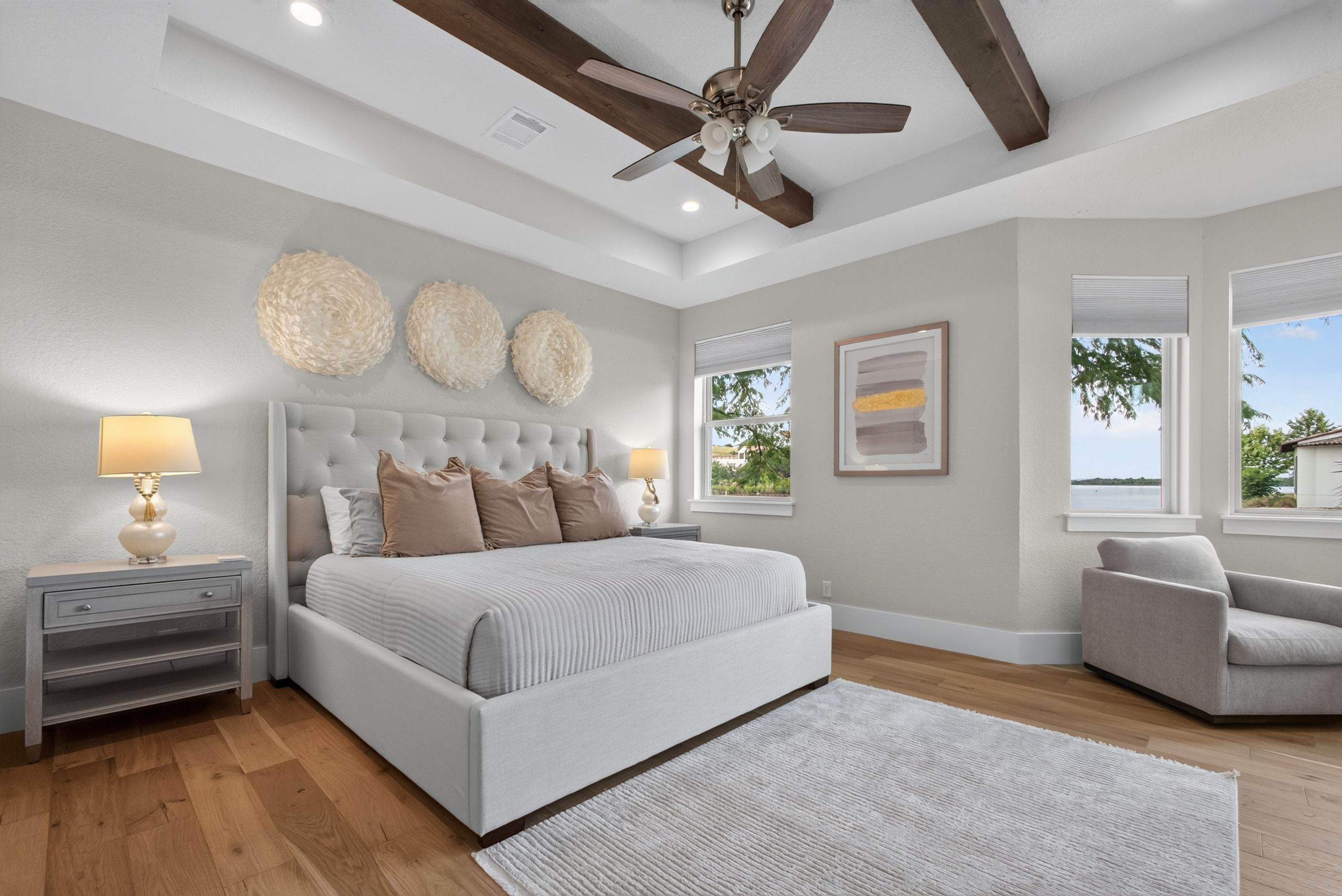 A bedroom with a large bed, a ceiling fan, a nightstand, a chair, and a window with a view.
