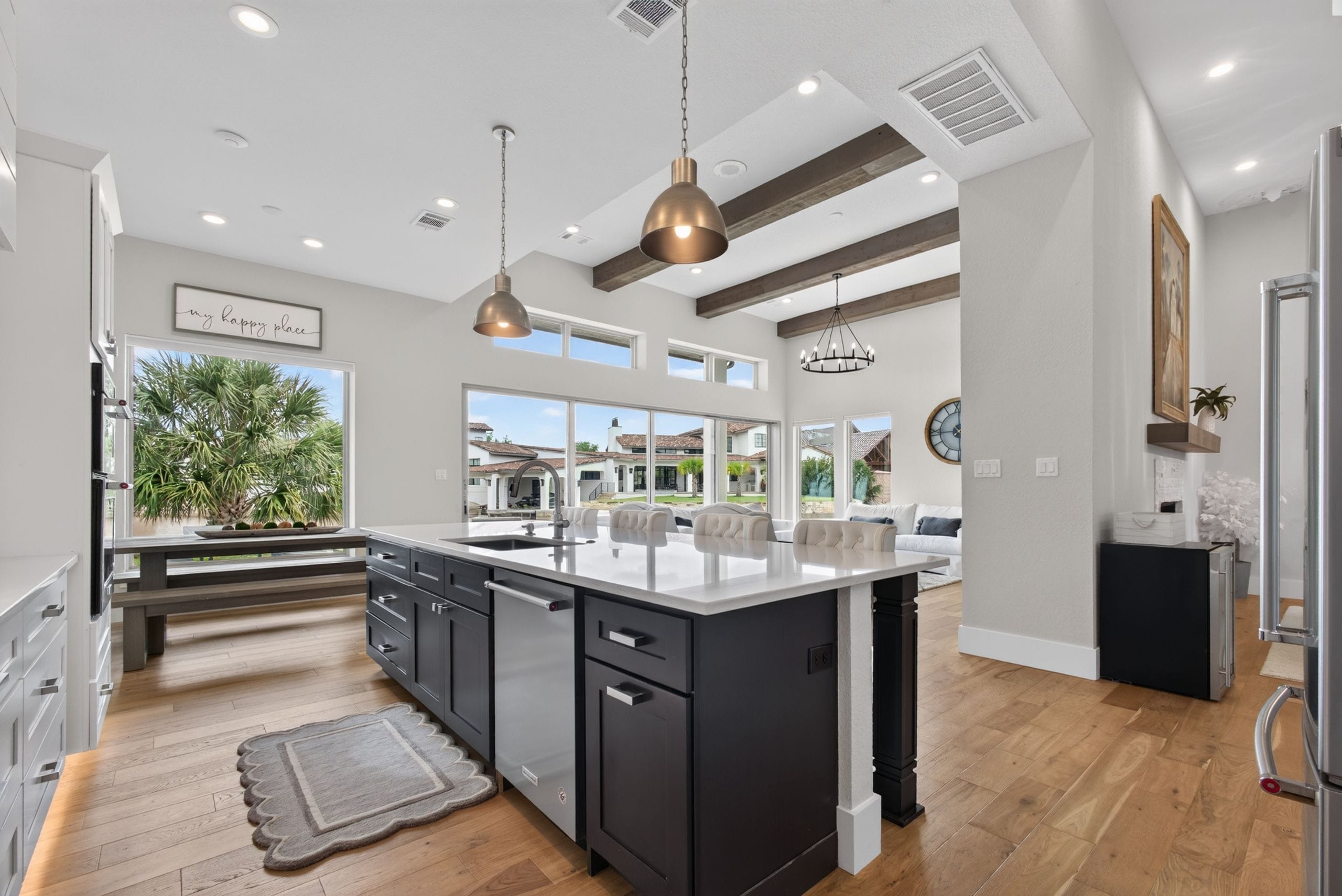 A modern kitchen with a large island, pendant lighting, and a view of the neighborhood.