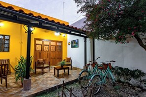 Un pati amb sòl de rajola, mobles de fusta, una bicicleta i plantes en testos.