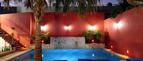 Una piscina con pared de piedra y paredes rojas, rodeada de sillas de descanso y plantas en macetas.