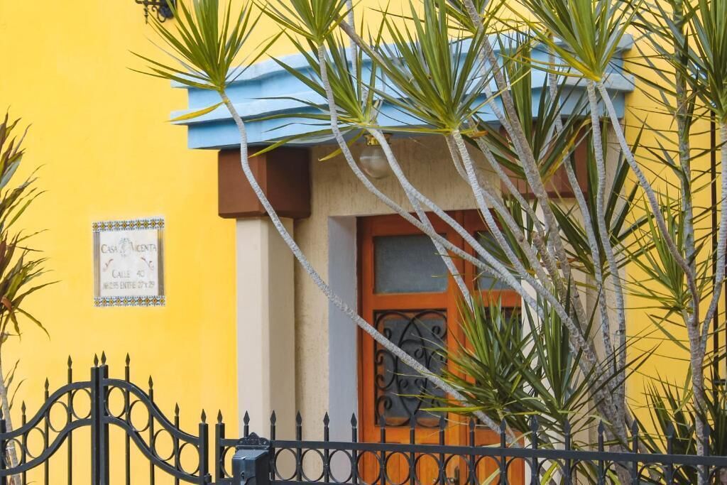 Un edificio amarillo con techo azul, puerta marrón y una verja de hierro negro.