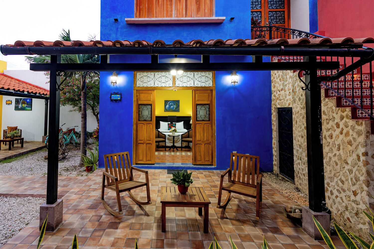 Um pátio com uma pérgola de madeira, duas cadeiras de balanço, uma pequena mesa e um vaso de planta.