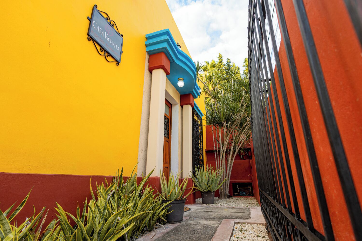 Um edifício amarelo vibrante com uma placa que diz 'CASA VICENTA' e um portão de metal preto.