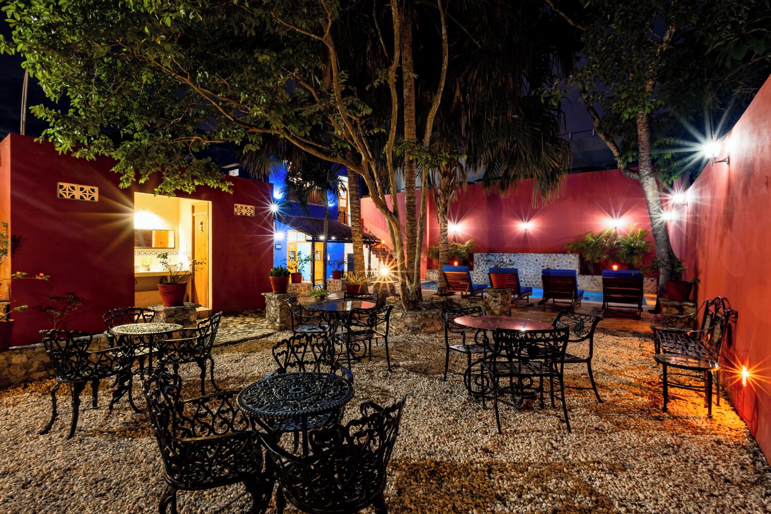 Un patio al aire libre con mesas y sillas, rodeado de muros rojos y árboles.