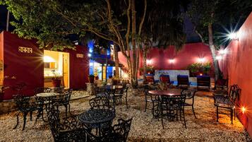 Un patio al aire libre con mesas y sillas, rodeado de muros rojos y árboles.