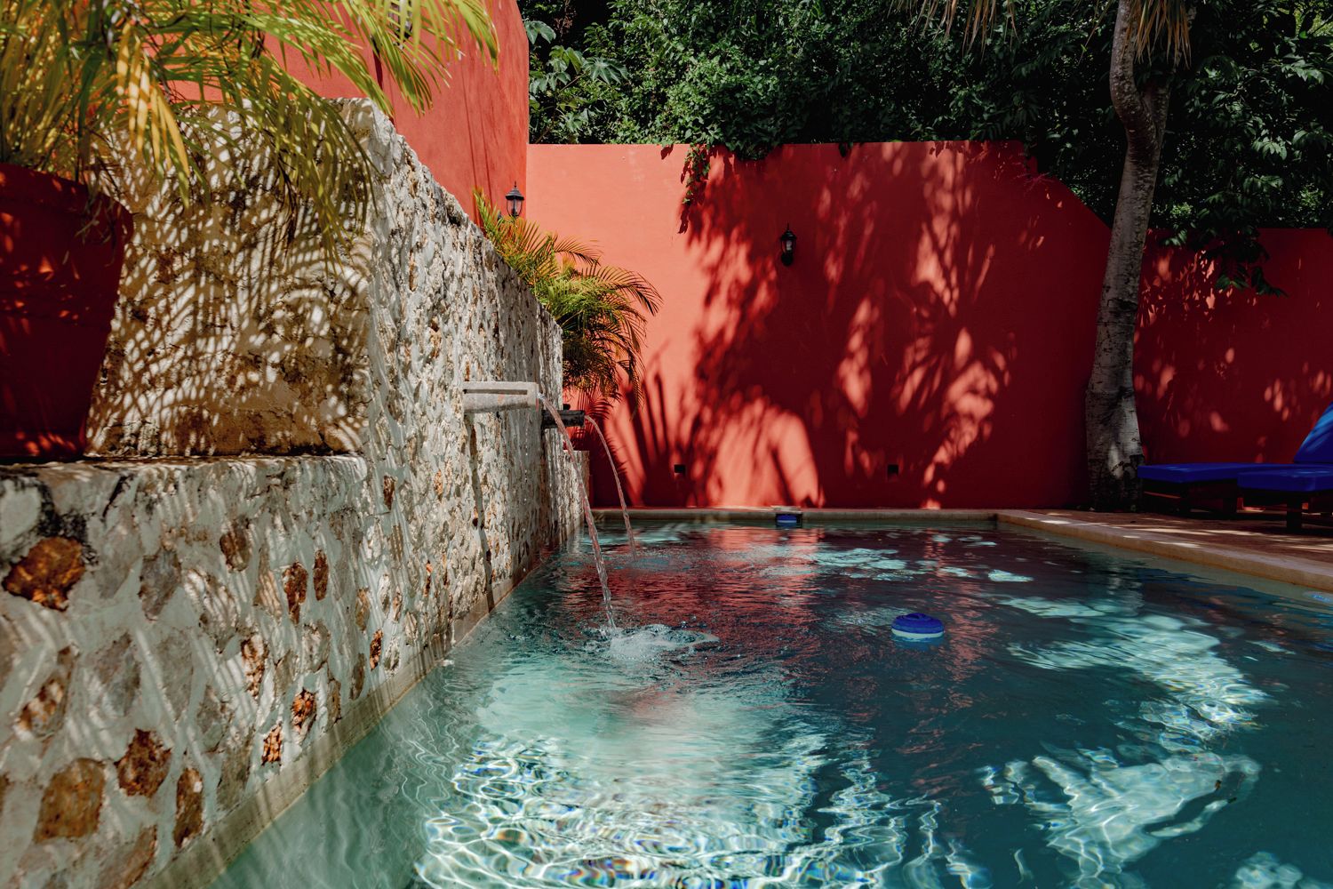 Una piscina con un muro de piedra y un muro rojo al fondo.