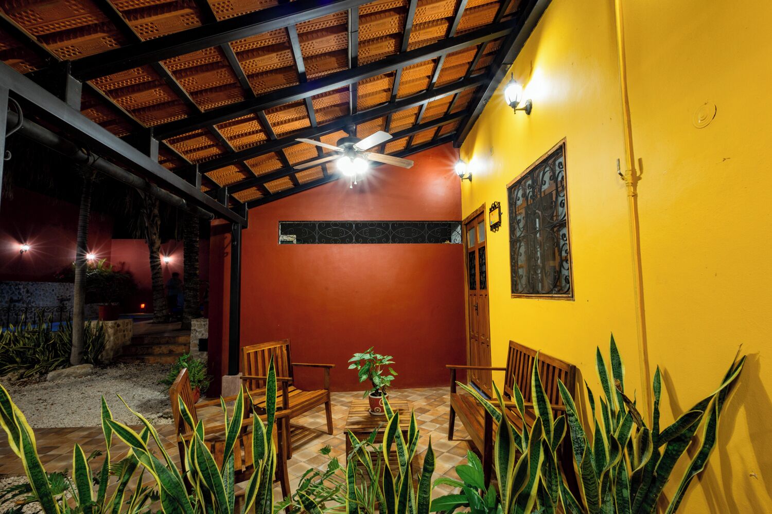 Un patio al aire libre con ventilador de techo, mobiliario de madera y plantas en macetas.