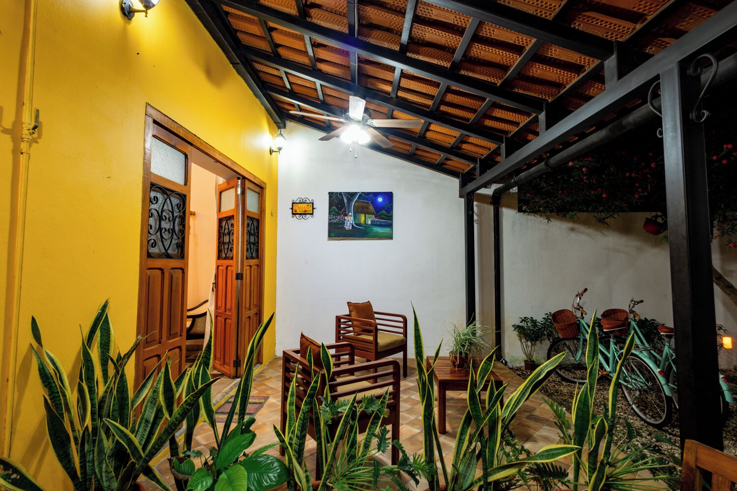 A room with a yellow wall, wooden furniture, a ceiling fan, and a painting.