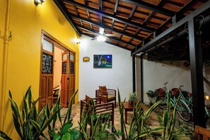 A room with a yellow wall, wooden furniture, a ceiling fan, and a painting. - Casa Vicenta (Izamal)