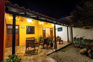 A courtyard with a tiled floor, wooden furniture, potted plants, and bicycles.