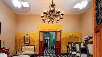 A hotel room with a chandelier, a dining area with chairs, a checkered floor, and a view through an open door.