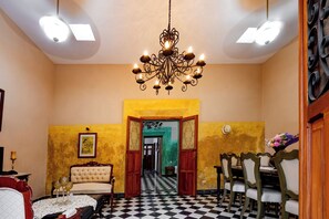 A hotel room with a chandelier, a dining area with chairs, a checkered floor, and a view through an open door. - Casa Vicenta (Izamal)