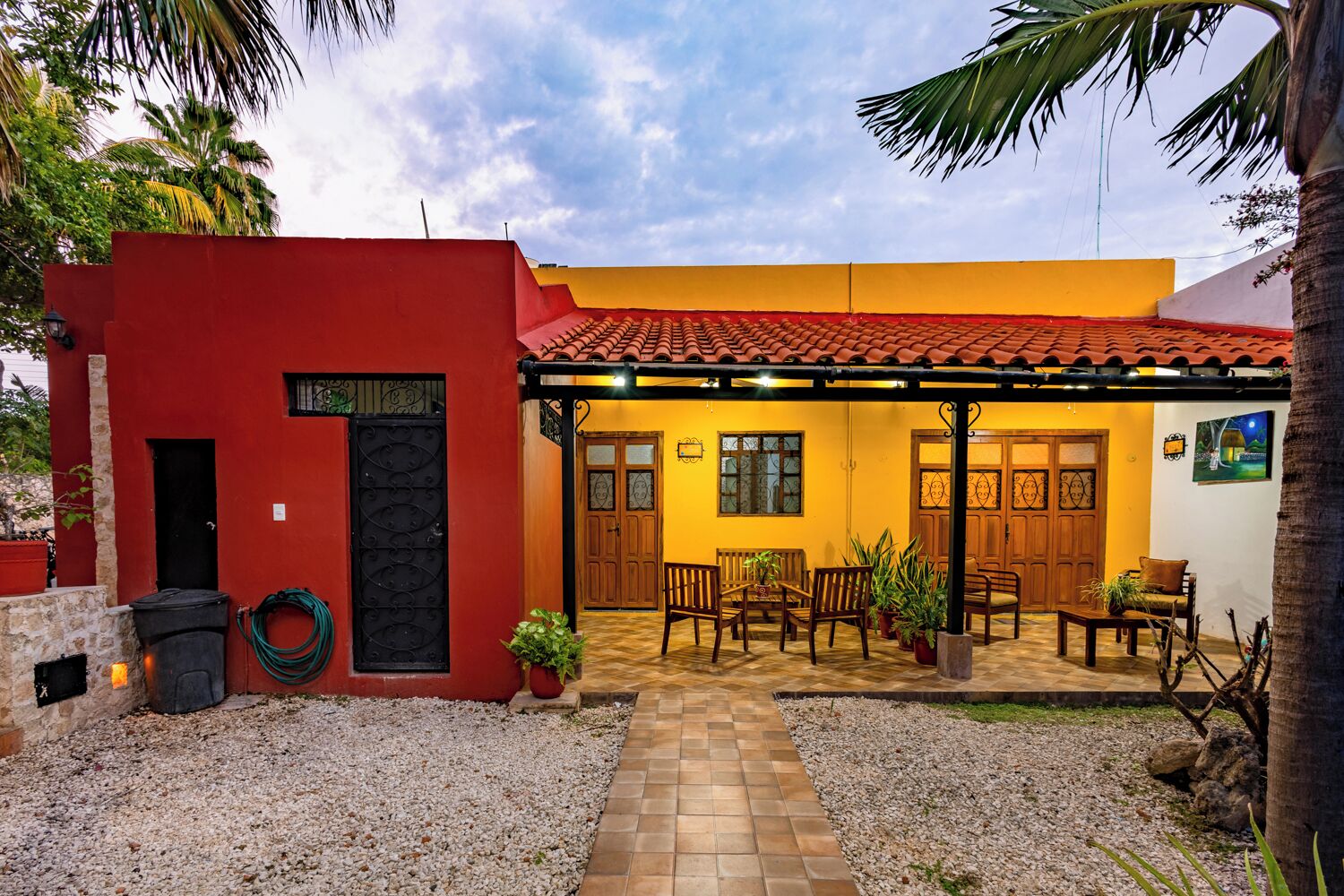 A two-story building with a red and yellow facade, a tiled roof, and a patio area with outdoor seating.