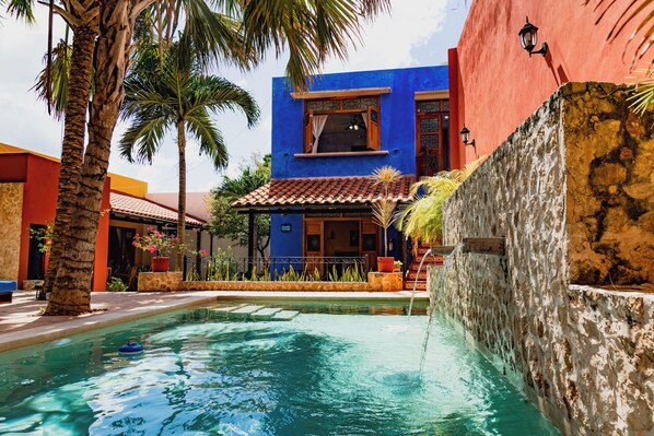 A pool area with a blue building, palm trees, and a stone wall.