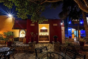 A courtyard with a stone bench, potted plants, and a building entrance with a wooden door.