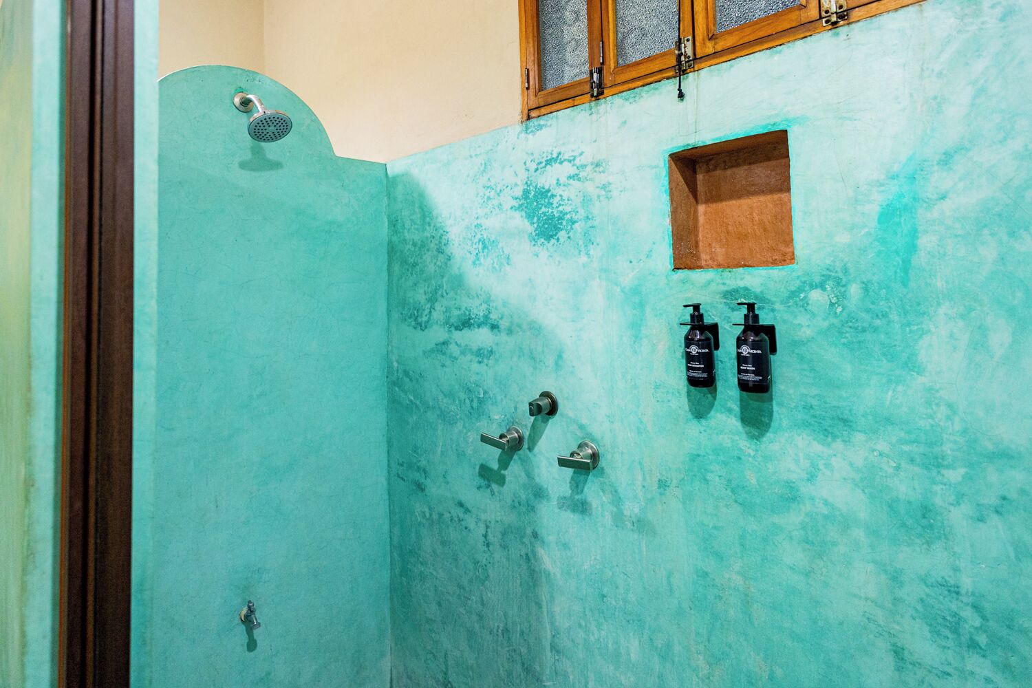 Un baño con una pared turquesa, un cabezal de ducha y dos botellas de champú.