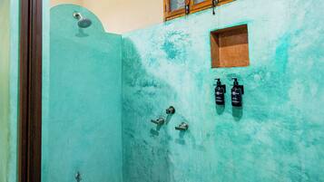 Un baño con una pared turquesa, un cabezal de ducha y dos botellas de champú.