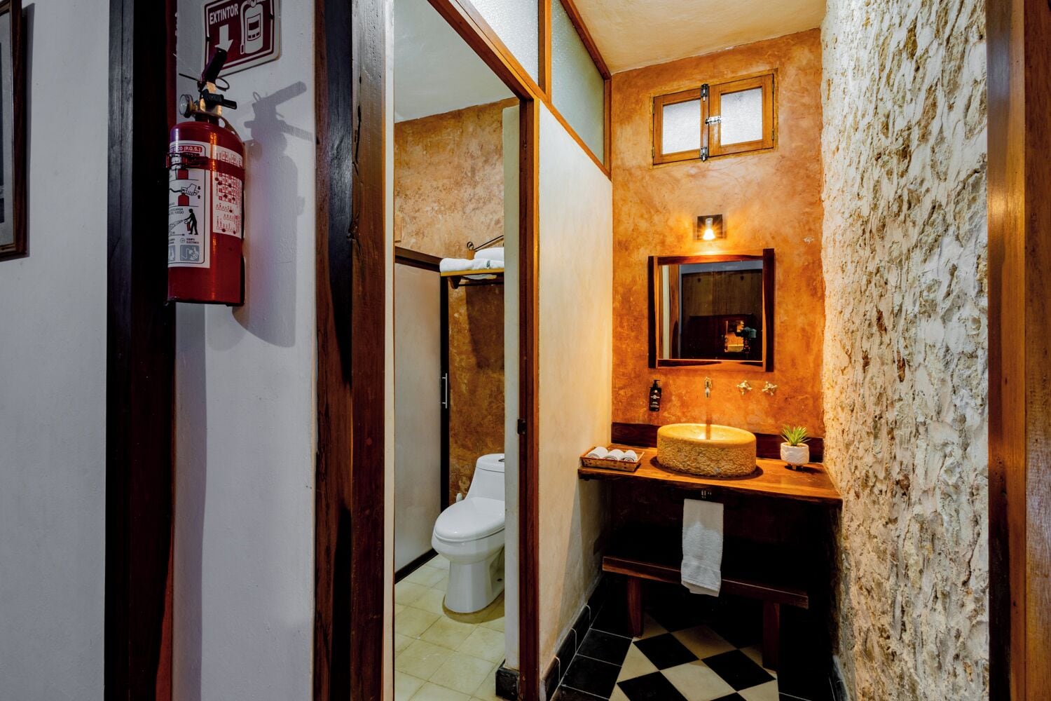Baño con inodoro, lavamanos, espejo y extintor.