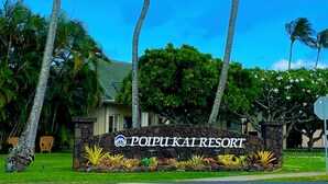 Schild für Poipui Kai Resort mit Palmen und einer Steinmauer.