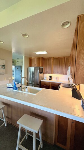 A kitchen with wooden cabinets, a stainless steel refrigerator, a sink, and a countertop. - Ocean Views • Dual Lanais & A/C • Walk to Beaches, Pools & Tennis @ BluEscape (Koloa)