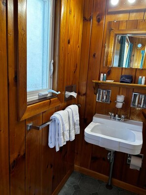 A wooden-paneled bathroom with a window, a sink, and a mirror.