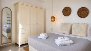 Ein Schlafzimmer mit einem Bett, einem Kleiderschrank, einem Spiegel und zwei gewebten Wandbildern.