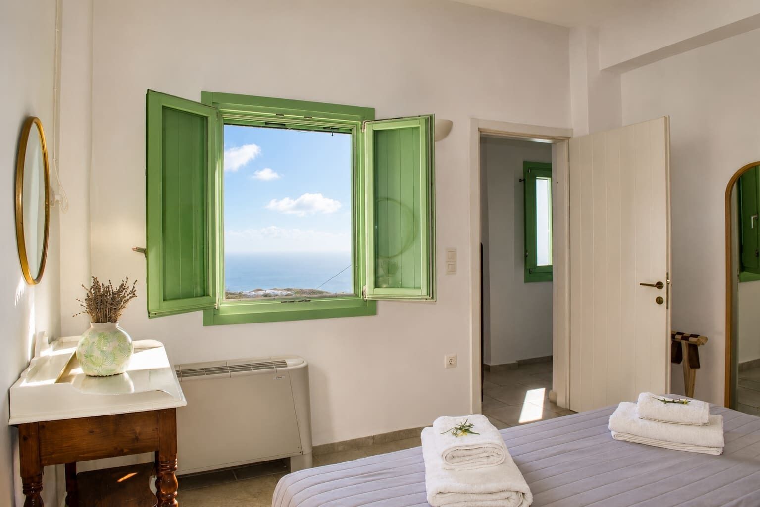 Een slaapkamer met uitzicht op zee, een radiator, een nachtkastje met een vaas, en een bed met handdoeken.