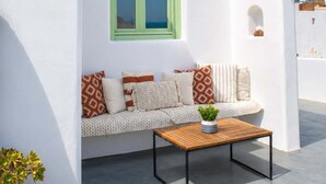 Ein weißes Gebäude mit einem grün gerahmten Fenster, ein Sofa mit gemusterten Kissen, ein Holztisch und ein Blumentopf.