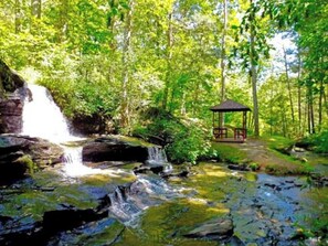 Ein Wasserfall, ein Pavillon und ein bewaldetes Gebiet.