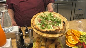 A kitchen with a pizza on a wooden board, a plate of bread rolls, and a fruit platter. - Porta Marina Resort Pompeii (Pompei)