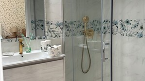 A bathroom with a glass-enclosed shower, a vanity with a mirror, and floral-patterned tiles. - Porta Marina Resort Pompeii (Pompei)