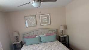 Ein Schlafzimmer mit einem Bett, zwei Nachttischen, einem Deckenventilator und zwei Wanddekorationen.