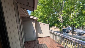 Eine Holzterrasse mit einer weißen Tür, einem weißen Zaun und Blick auf geparkte Autos und Bäume.